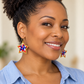 Woman in a light blue shirt wearing gold hoops with red, white, and blue beaded star charms edged in gold.