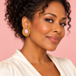 Woman wearing light pink oval cat-eye stud earrings with textured gold surrounds against a blush pink background.