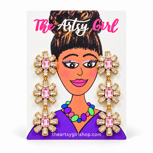 Three-tier floral earrings with light pink center stones, clear crystal petals, and gold settings on an Artsy Girl card.