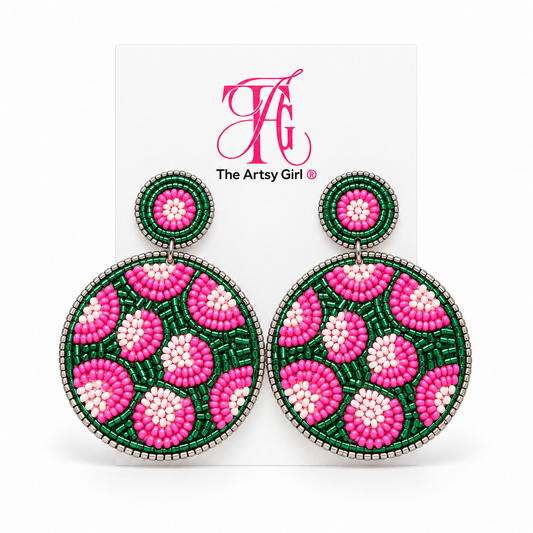 Round pink and green beaded leopard earrings with silver edging displayed on The Artsy Girl card.