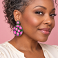 Woman wearing round pink and green beaded leopard earrings with a cream blouse against a blush pink background.