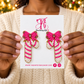 Woman holding The Artsy Girl card with pink and white beaded candy cane earrings topped with pink bows.