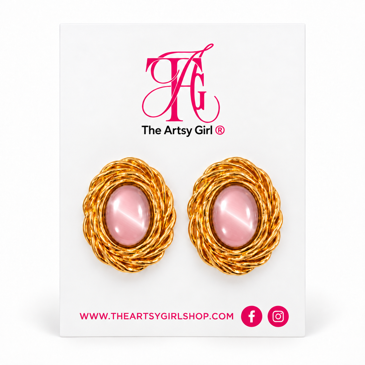 A pair of gold-toned twisted wire earrings with oval pink cabochon centers, displayed on a white jewelry card branded The Artsy Girl.