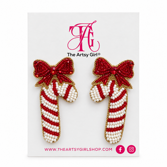 Red and white beaded candy cane earrings with red bows and gold edging on The Artsy Girl card against a white background.
