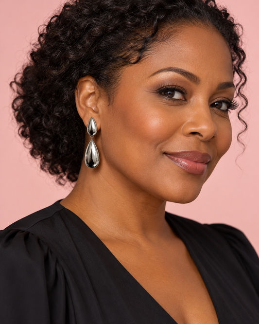 Woman wearing polished silver double-teardrop earrings with a black blouse against a blush pink background.