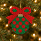 Green beaded Christmas bulb ornament with red polka dots, a red bow and gold accents hanging on a tree with warm white lights.
