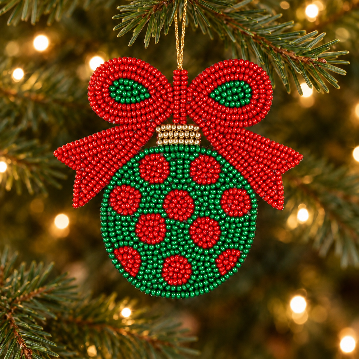 Green beaded Christmas bulb ornament with red polka dots, a red bow and gold accents hanging on a tree with warm white lights.