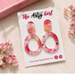 Pink floral earrings on a 'The Artsy Girl' branded card with flowers around.