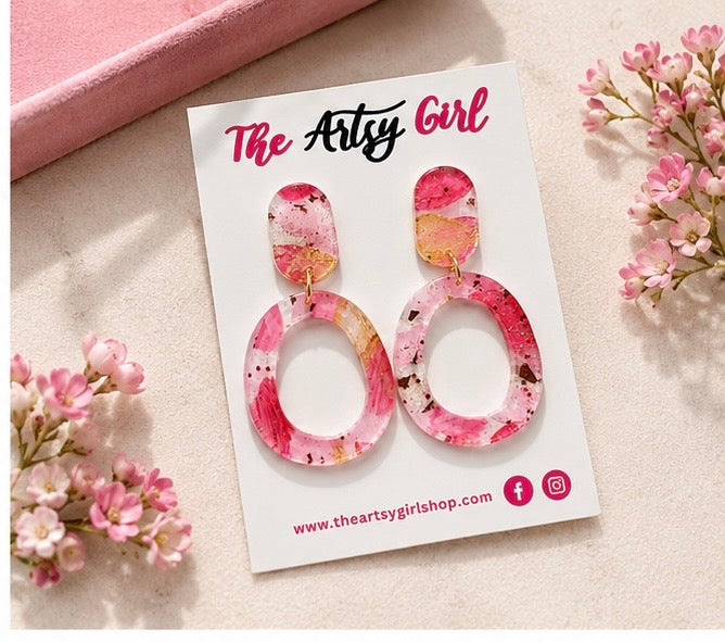 Pink floral earrings on a 'The Artsy Girl' branded card with flowers around.